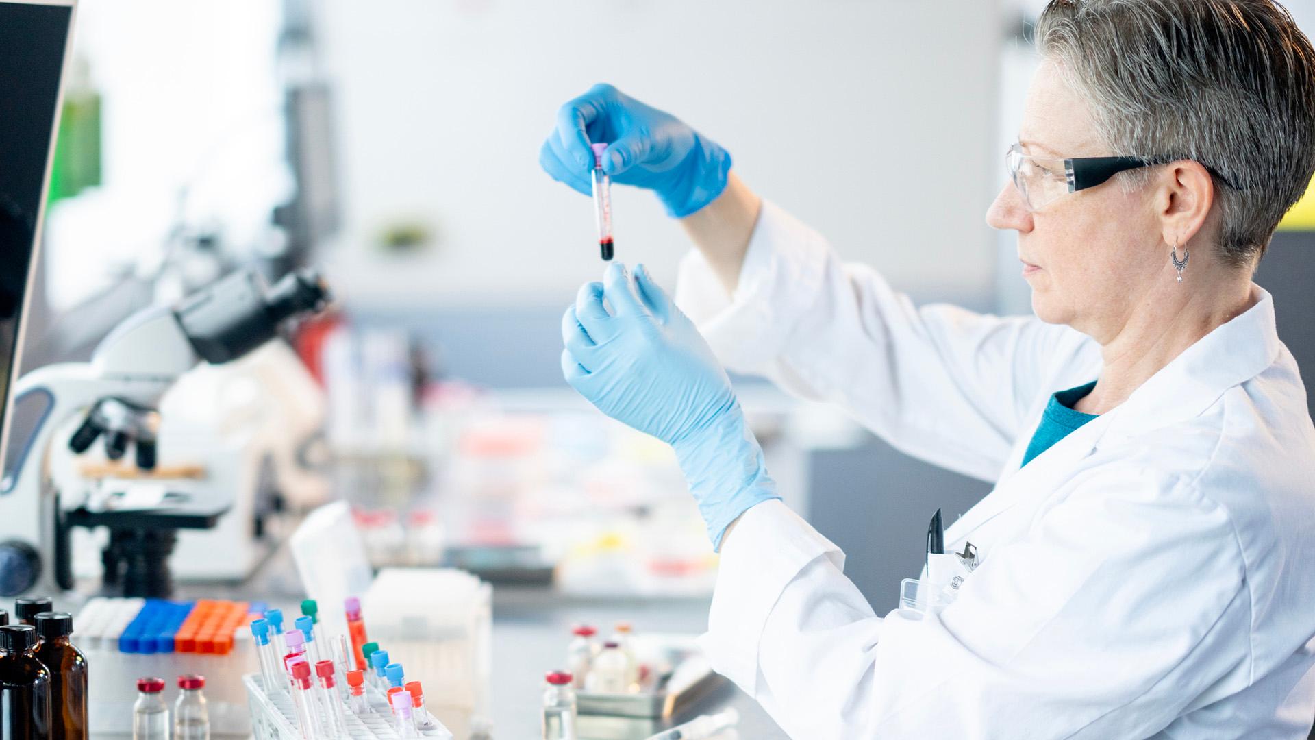 A female medical laboratory technician works independently as she analyzes plasma samples. She is wearing a lab coat as well as protective eyewear and gloves as she focuses on her task.