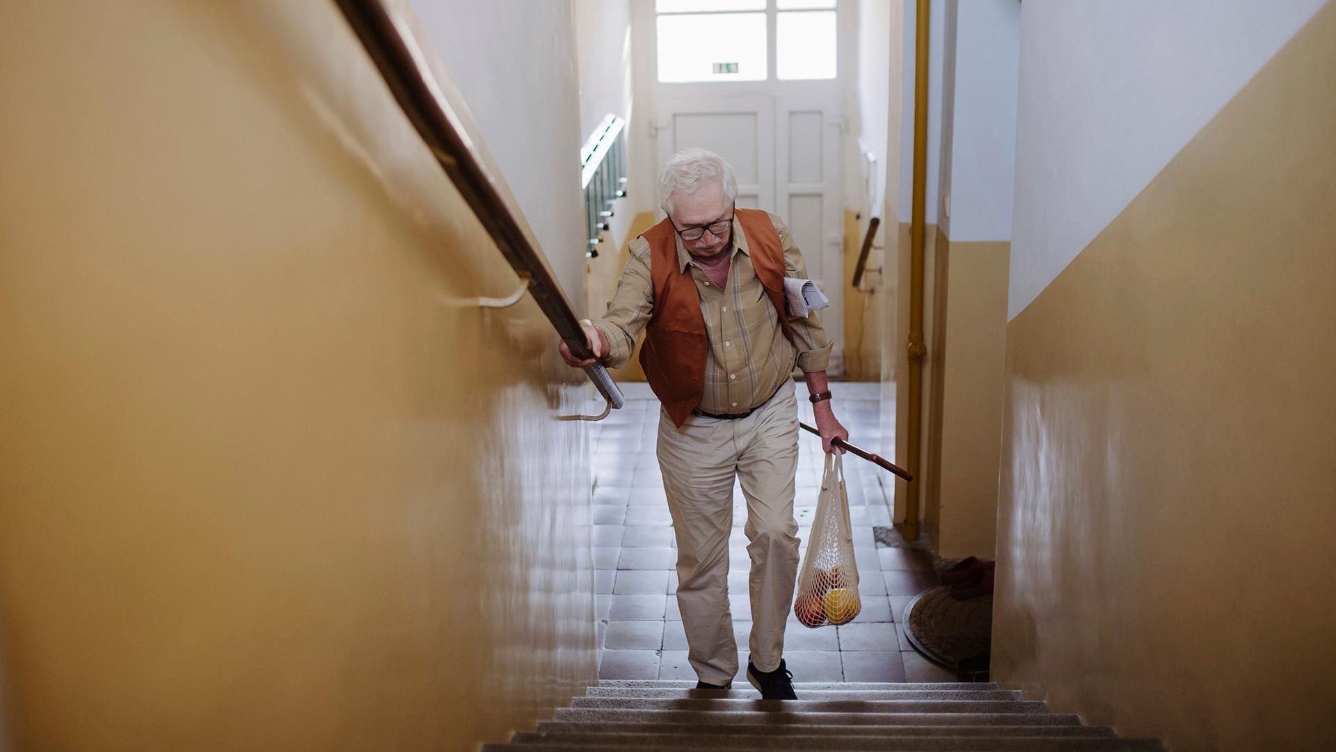 Senior man moving up with bag of fruits on staircase